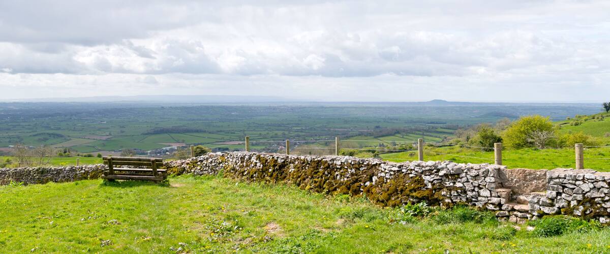 A stone wall with a wooden bench overlooking a green valley.