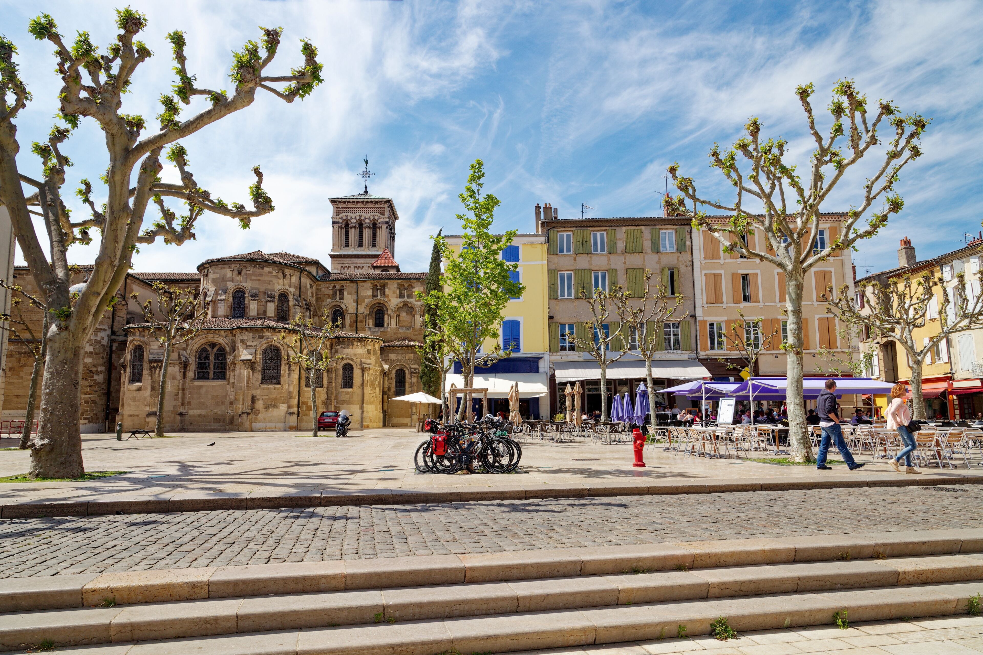 A historic square with a church, trees, and buildings with cafes.