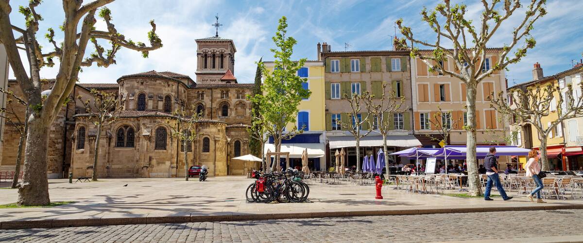 A historic square with a church, trees, and buildings with cafes.