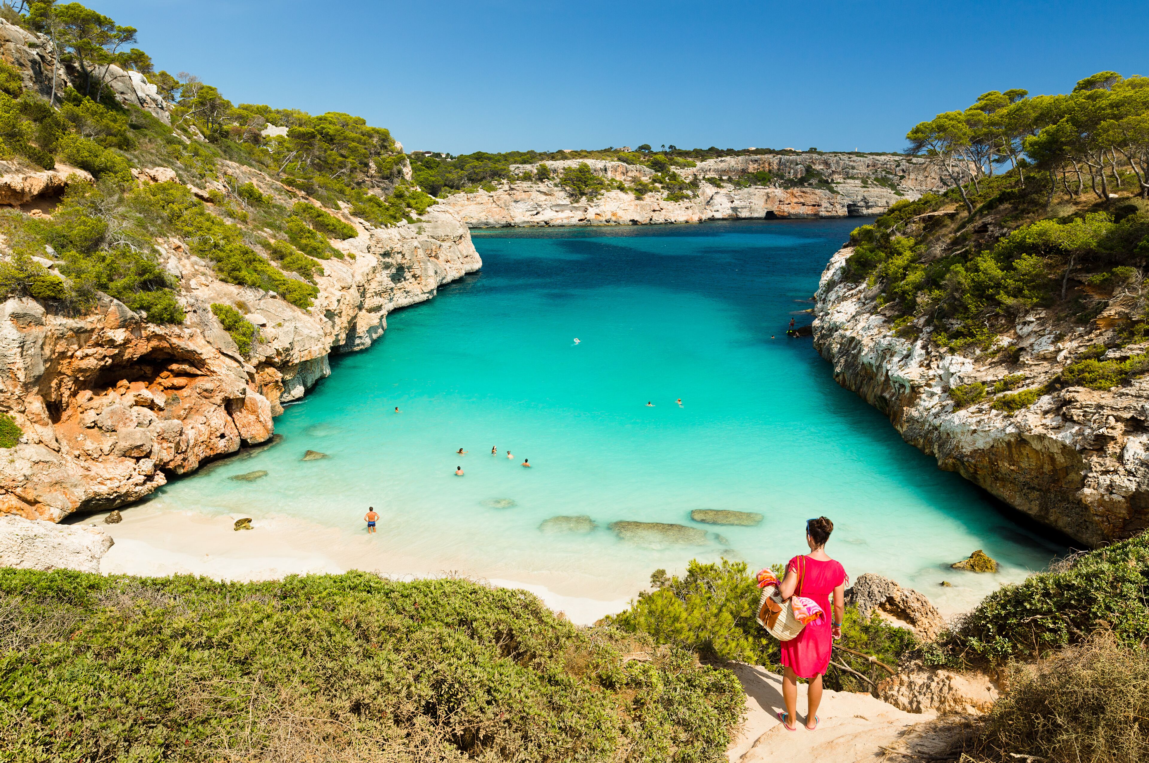 A coastal landscape with a clear turquoise sea, rocky cliffs, and a sandy beach.