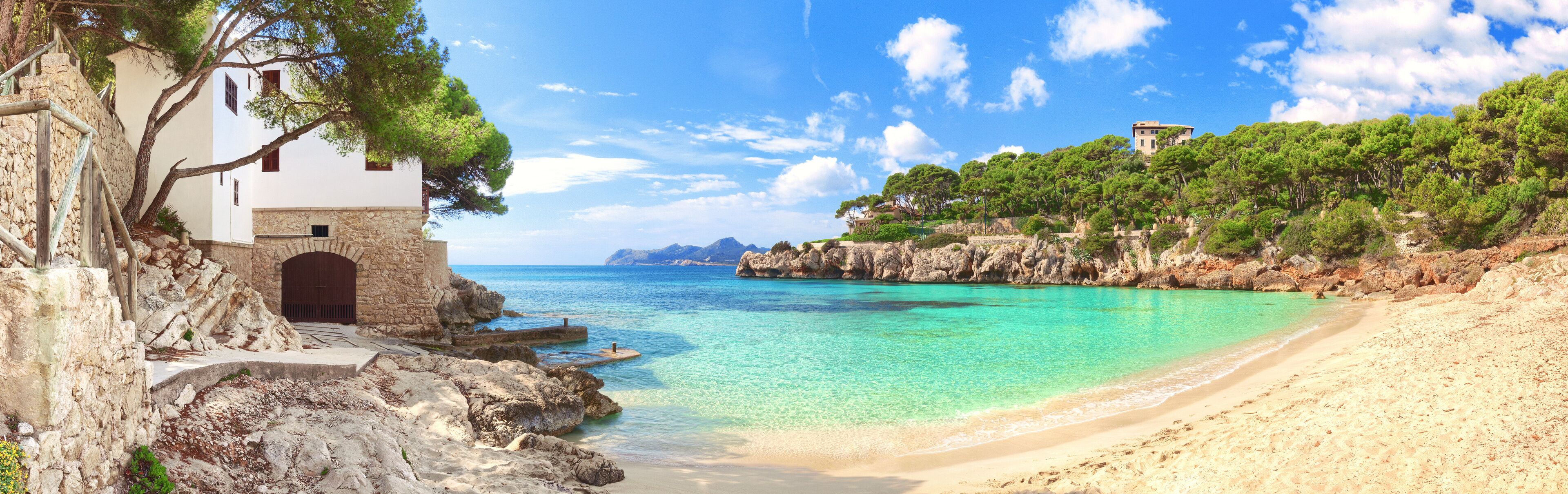A coastal landscape with a white building, clear turquoise waters, and rocky cliffs.