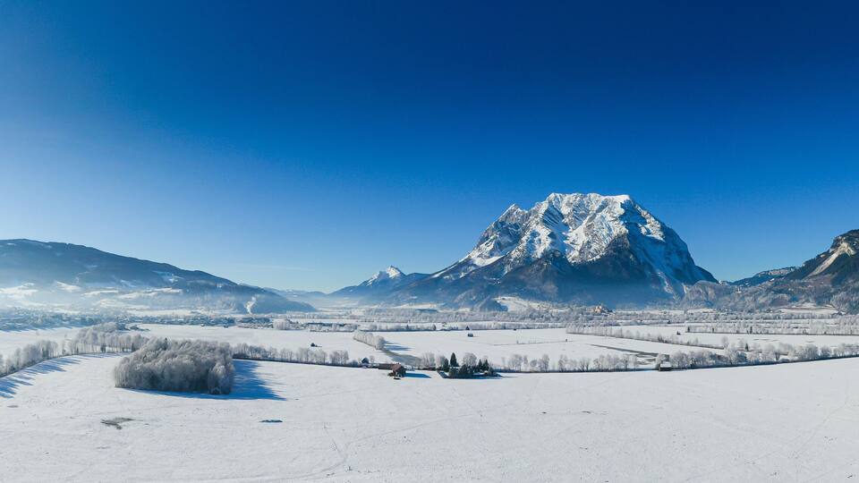 A snow-covered landscape with a prominent mountain peak, a river, and scattered trees.