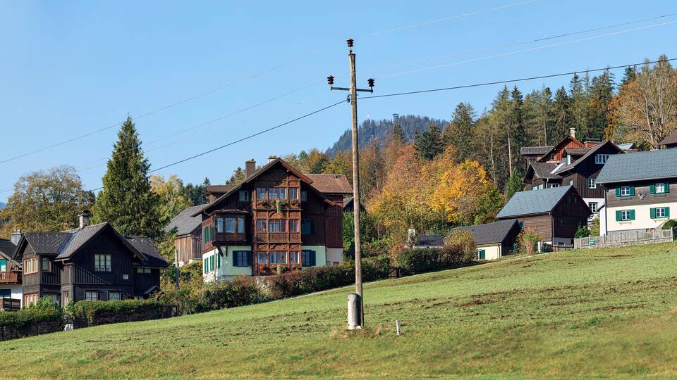 A hillside with traditional wooden houses, a utility pole, and a mountain in the background.