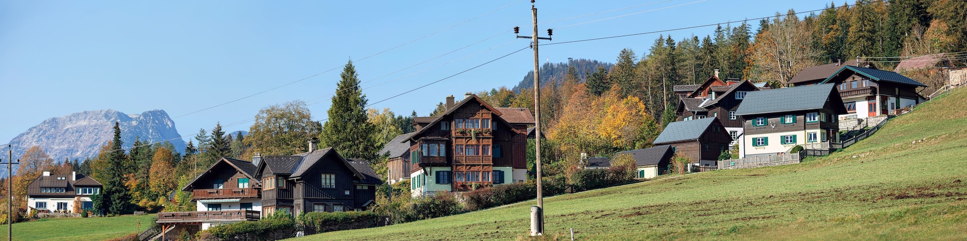 Uma encosta com casas de madeira tradicionais, um poste de eletricidade e uma montanha ao fundo.