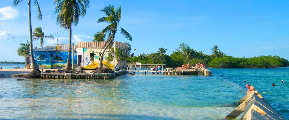 A beach with a colorful building, palm trees, and a pier extending into the water.