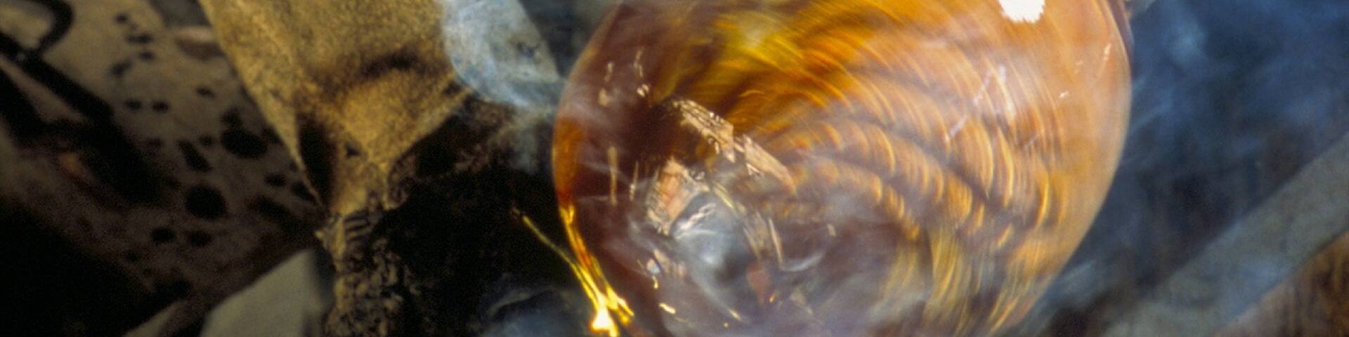 A glass object with a reflective surface, possibly a sculpture or decorative item, surrounded by smoke or steam.