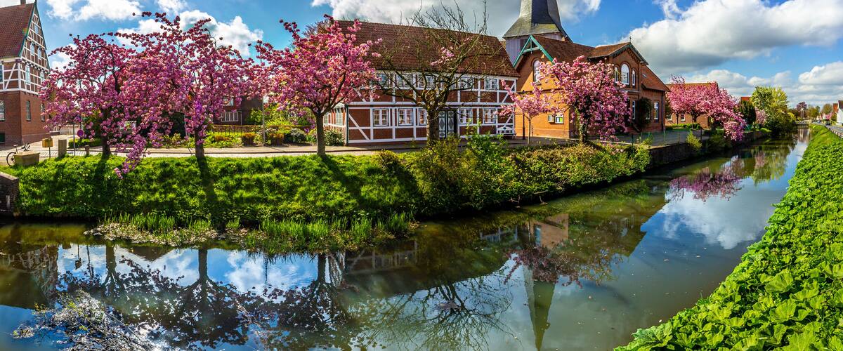 A canal with reflections, a church with a tall steeple, and blooming cherry trees.
