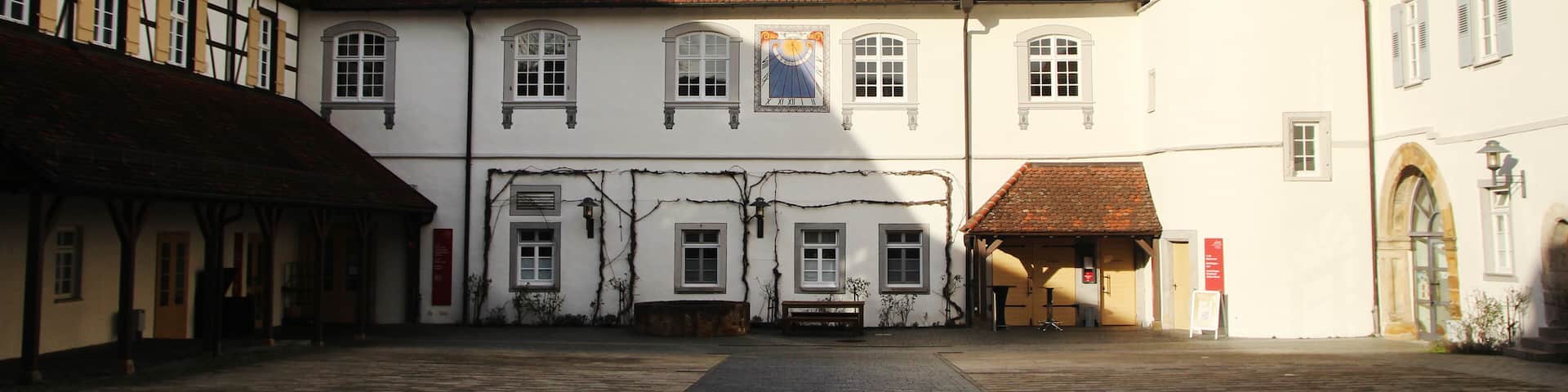 A historic courtyard with cobblestone pavement, traditional half-timbered buildings, and a white building with a rounded corner.