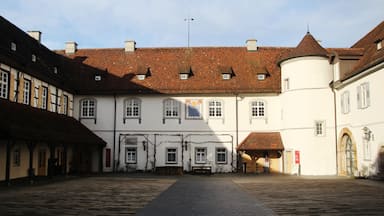 Um pátio histórico com pavimento de pedra, edifícios tradicionais de enxaimel e um edifício branco com esquina arredondada.