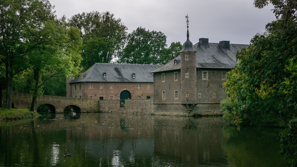 A historic building with a bridge over a river, surrounded by trees.