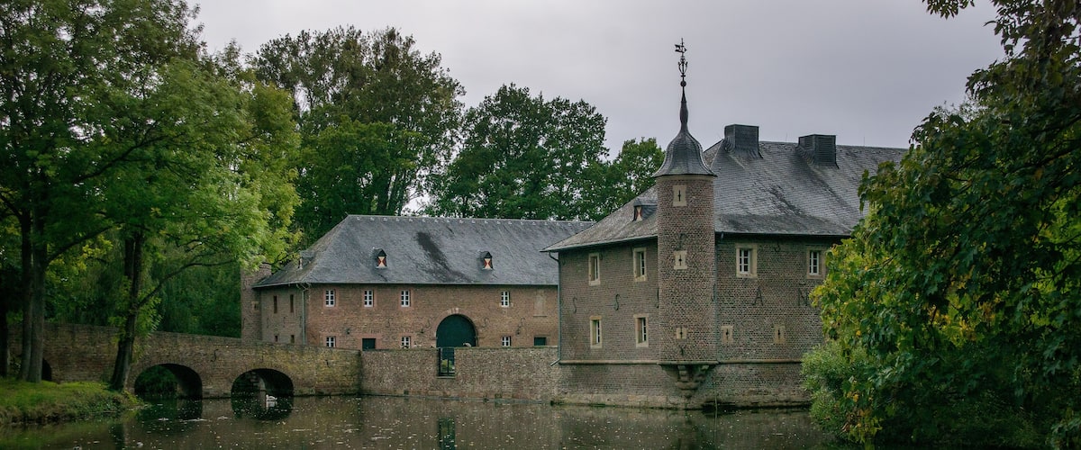 A historic building with a bridge over a river, surrounded by trees.