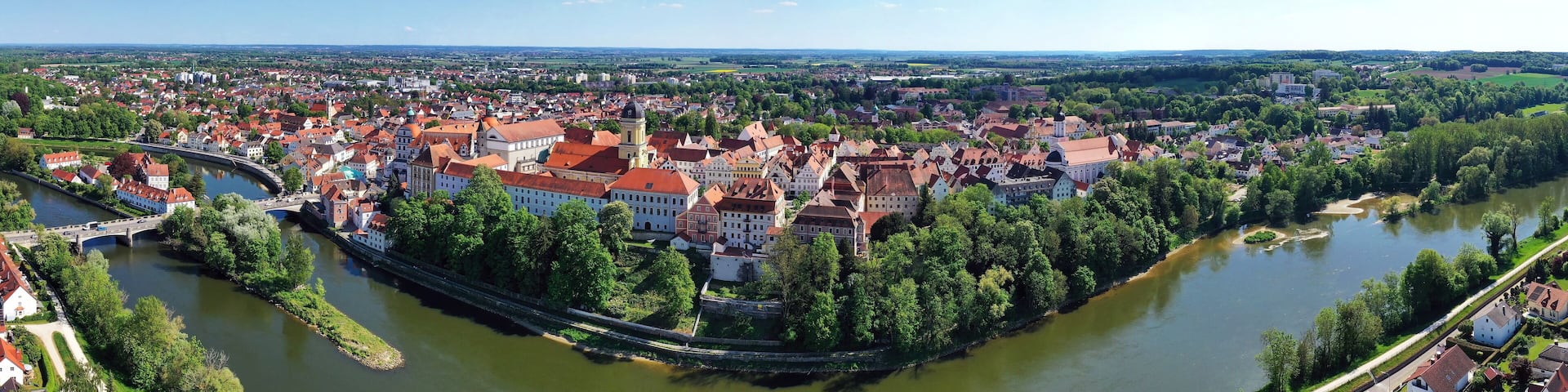 Eine beeindruckende Luftaufnahme von Neuburg an der Donau, einer malerischen Stadt in Bayern, Deutschland. Die Donau schlängelt sich durch die Stadt und bildet eine kleine Insel.