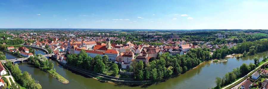 Ein Fluss schlängelt sich durch eine historische Stadt mit roten Dächern und einer Brücke.