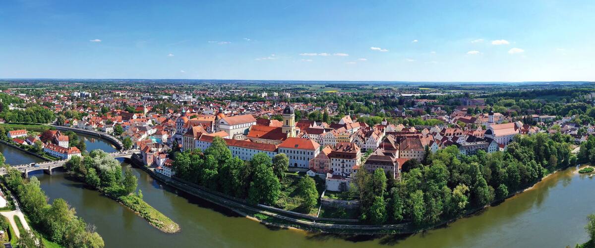 A river winding through a historic town with red-roofed buildings and a bridge.