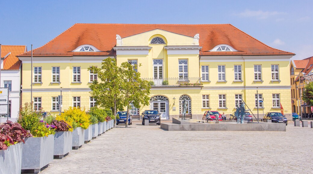 A yellow building with a red roof, surrounded by a cobblestone square and flower planters.