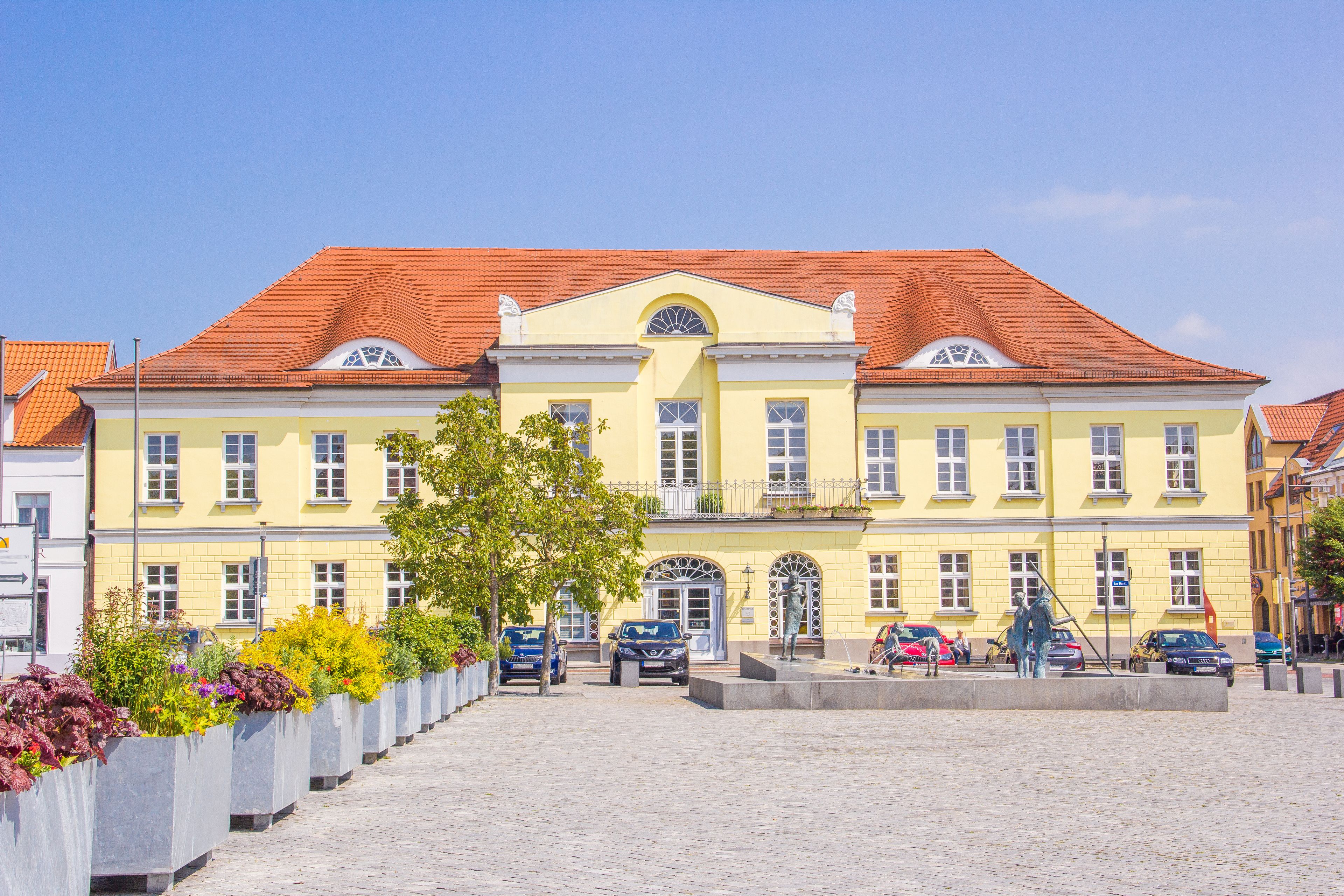 A yellow building with a red roof, surrounded by a cobblestone square and flower planters.
