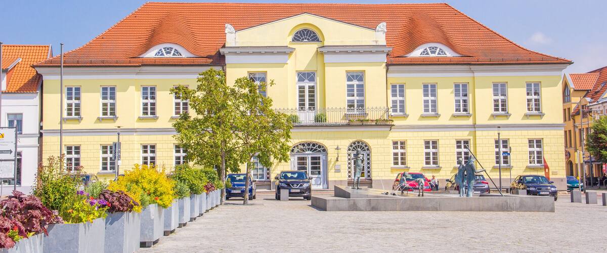 A yellow building with a red roof, surrounded by a cobblestone square and flower planters.