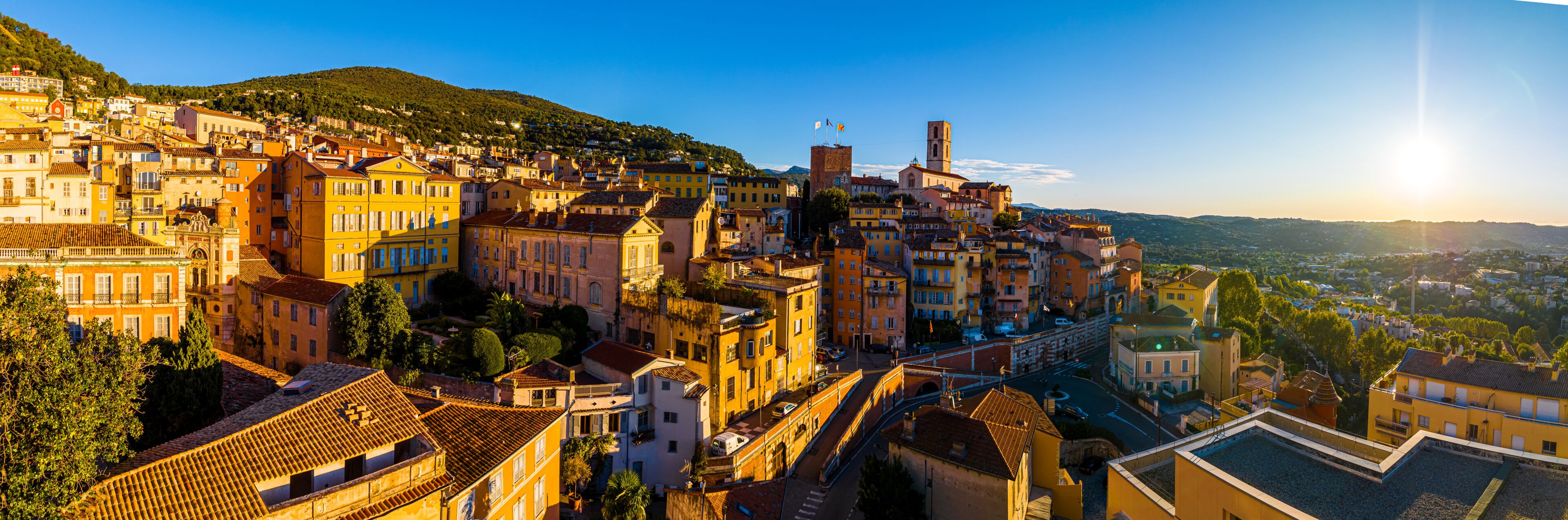 A historic town with terracotta-roofed buildings, a prominent church, and a hill in the background.