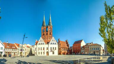 A historic town square with a prominent church featuring twin spires, surrounded by traditional European architecture.