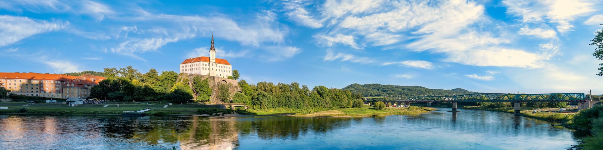Panoramic view of the historic residence and railway bridge over the Elbe River under a blue summer sky in northern Bohemia, Czechia