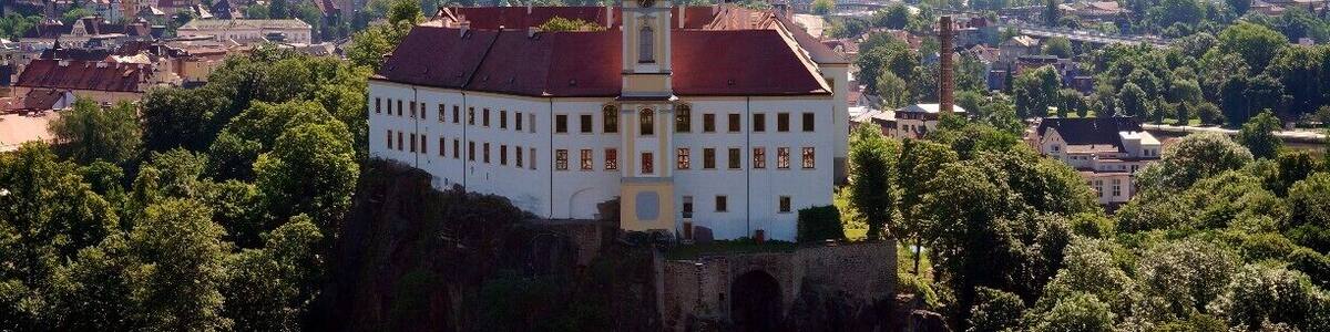 A castle on a hill overlooking a town with a church spire in the background.