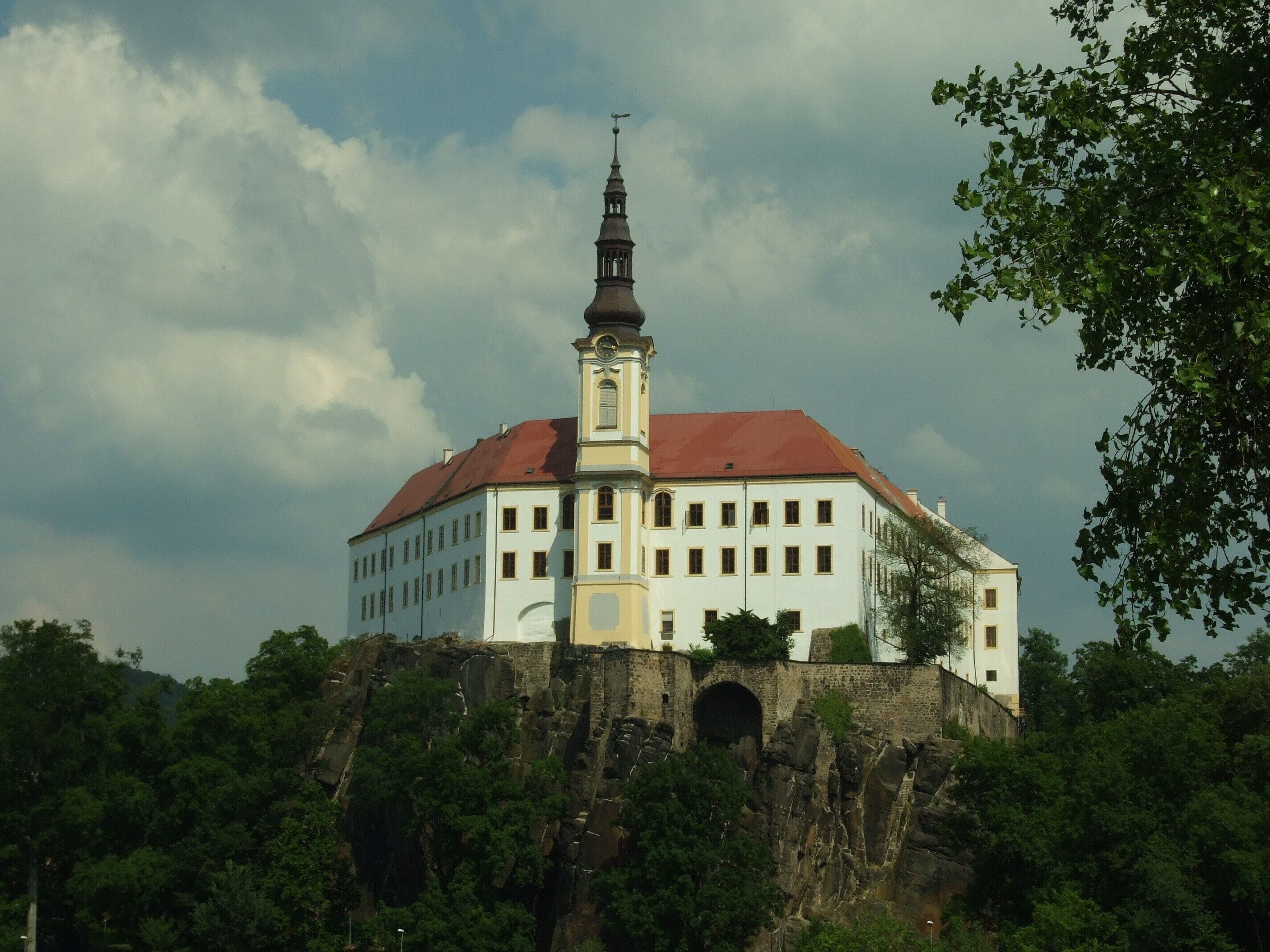 A white building with a red roof and a tower on a rocky hill.