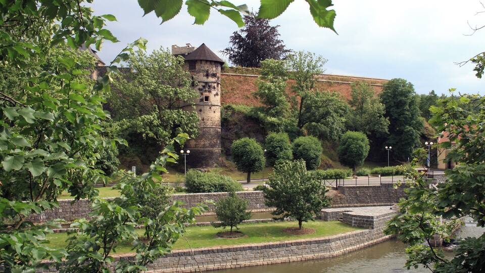 A historic tower surrounded by lush greenery and a calm water body.