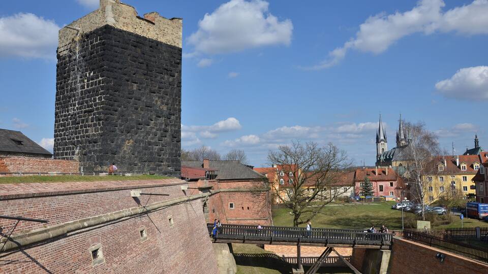 A historic brick tower, a wooden bridge, and a church with a spire.