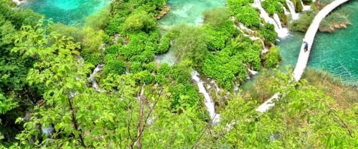 A lush green landscape with a turquoise river, a white bridge, and a rocky cliff.