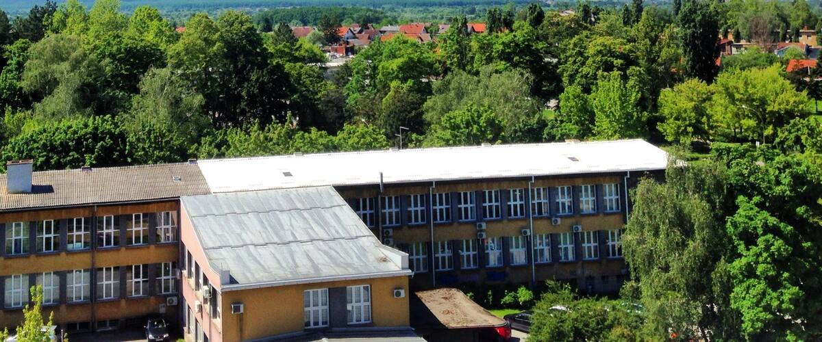 A multi-story building with a flat roof, surrounded by lush green trees and a clear blue sky.