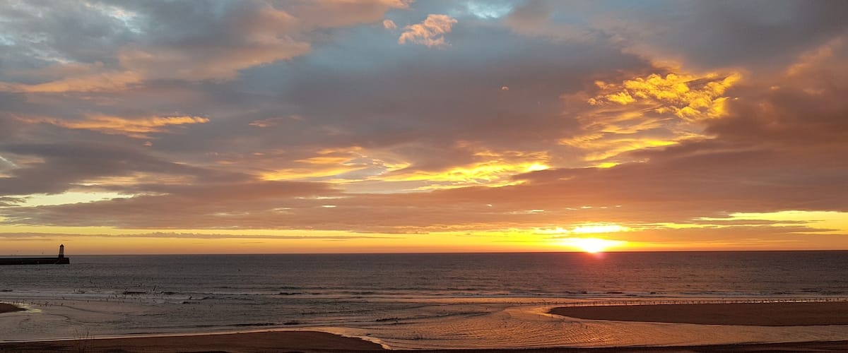 A sunset over a beach with a lighthouse in the distance.