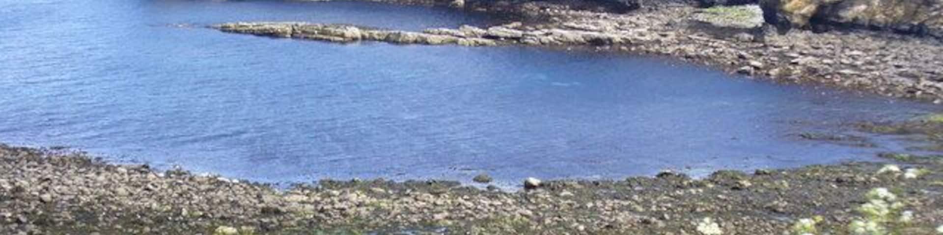 By Little Clett, Brough The bay near low tide seen from the road to Dunnet Head. The cliffs are layered old red sandstone and the shore is rocky.