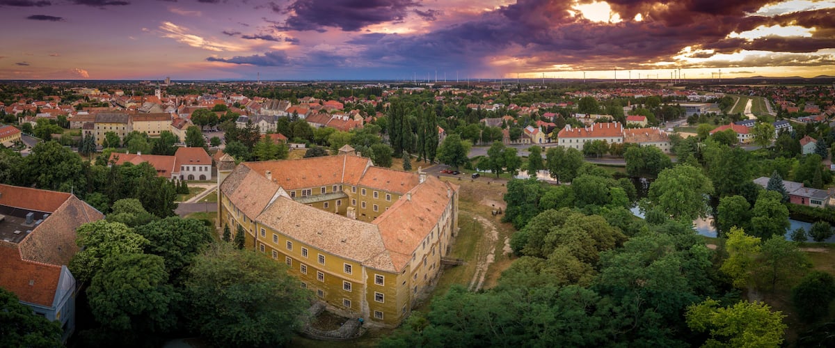 A town with historic buildings, a river, and a sunset sky.