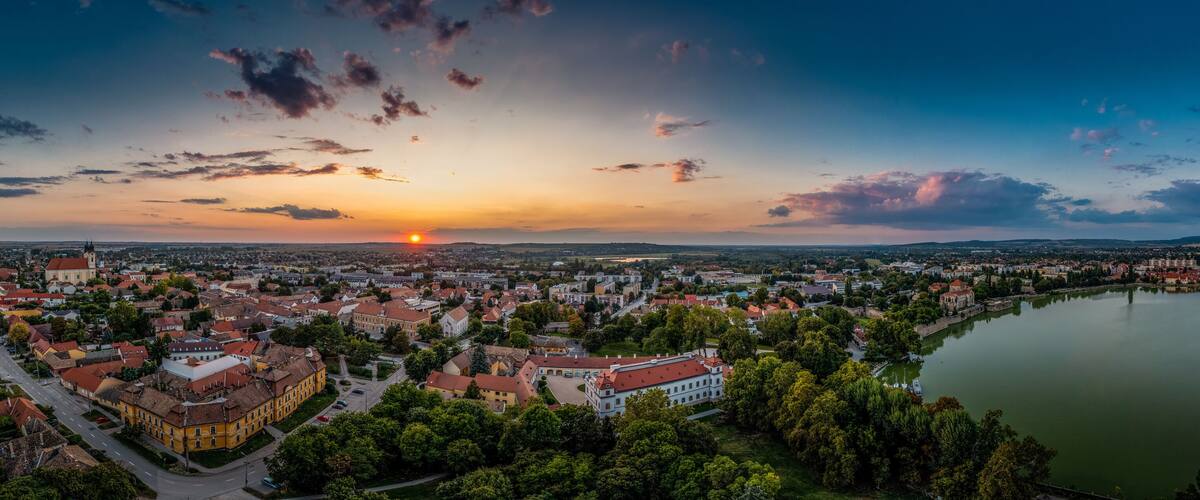 A panoramic view of a city at sunset with a river and a prominent church.