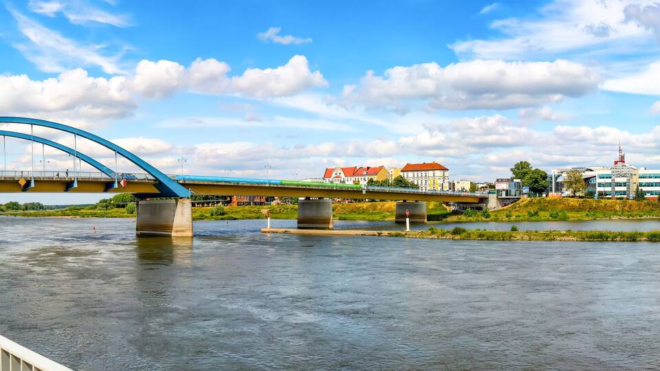 A river with a blue bridge, a brick walkway, and buildings in the background.
