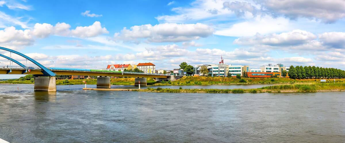A river with a blue bridge, a brick walkway, and buildings in the background.