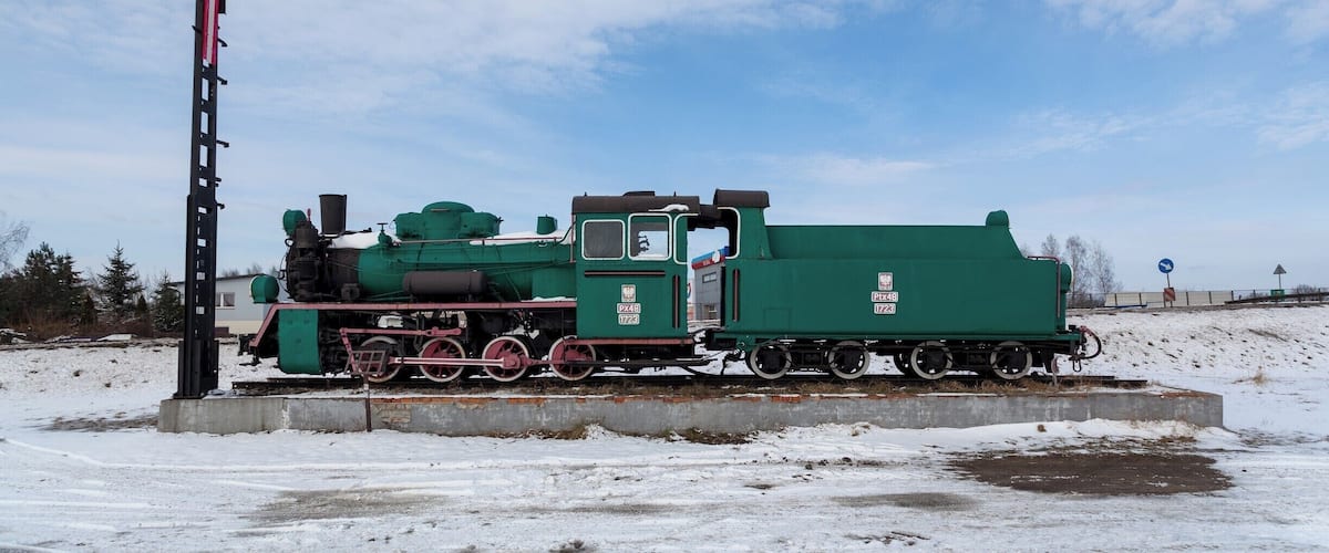 A green steam locomotive with a solar panel on a snowy platform.