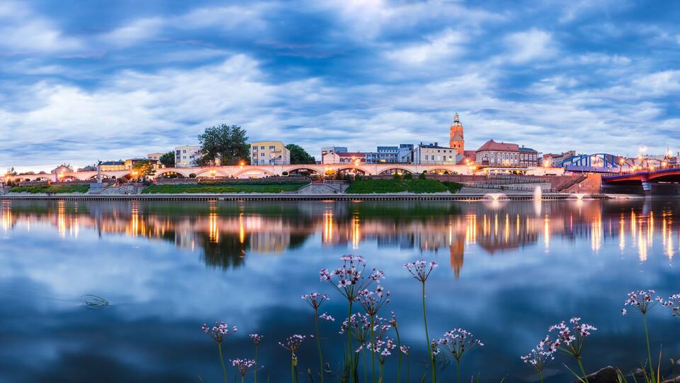 A cityscape with a river, a bridge, and a tower reflecting in the water.