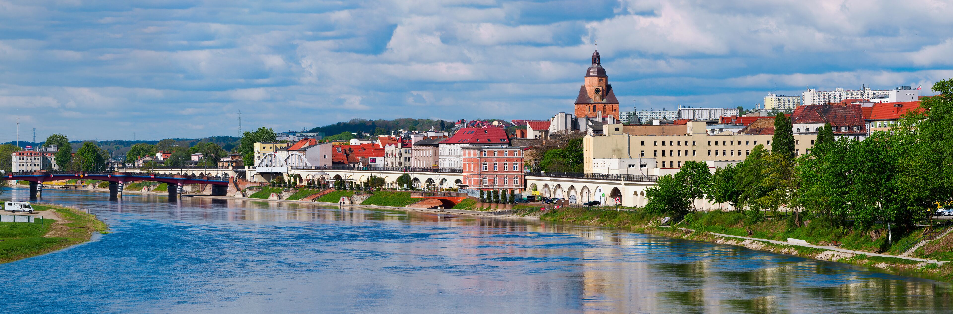 A river with a bridge, a prominent church tower, and a mix of historic and modern buildings along the riverbank.