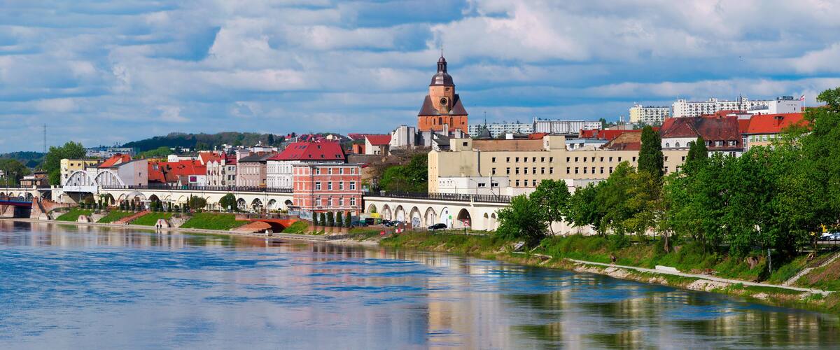 A river with a bridge, a prominent church tower, and a mix of historic and modern buildings along the riverbank.
