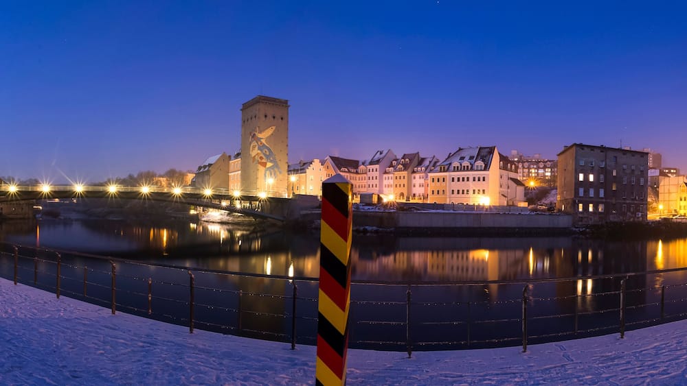 A snow-covered river with a bridge and illuminated buildings in the background.