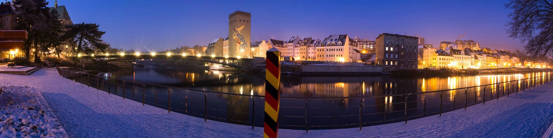 A snow-covered river with a bridge and illuminated buildings in the background.