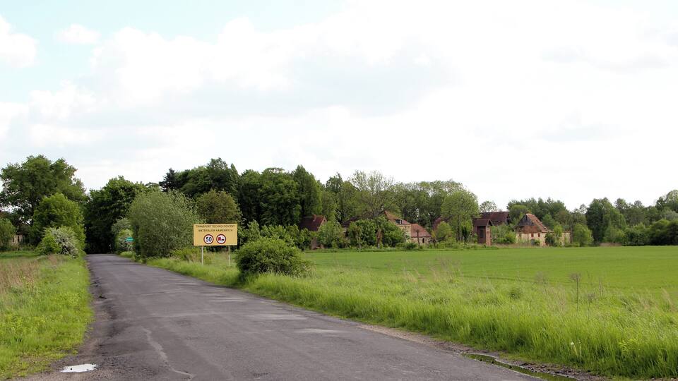 A rural road with a speed limit sign, surrounded by fields and houses.