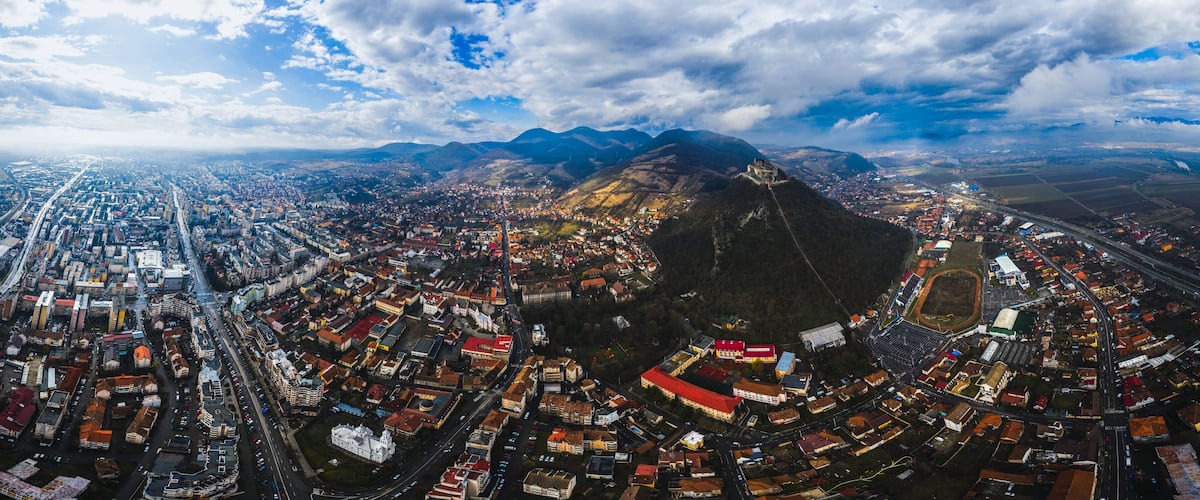 An aerial view of a city with a prominent mountain in the background, a large stadium, and a dense urban area with many buildings and roads.