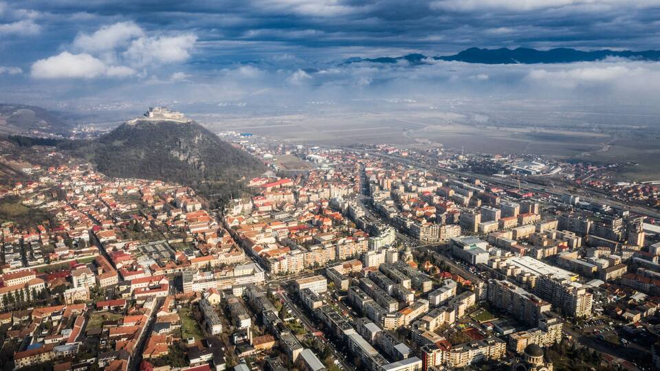 An aerial view of a city with a prominent castle on a hill, dense urban areas, and a mix of historical and modern architecture.
