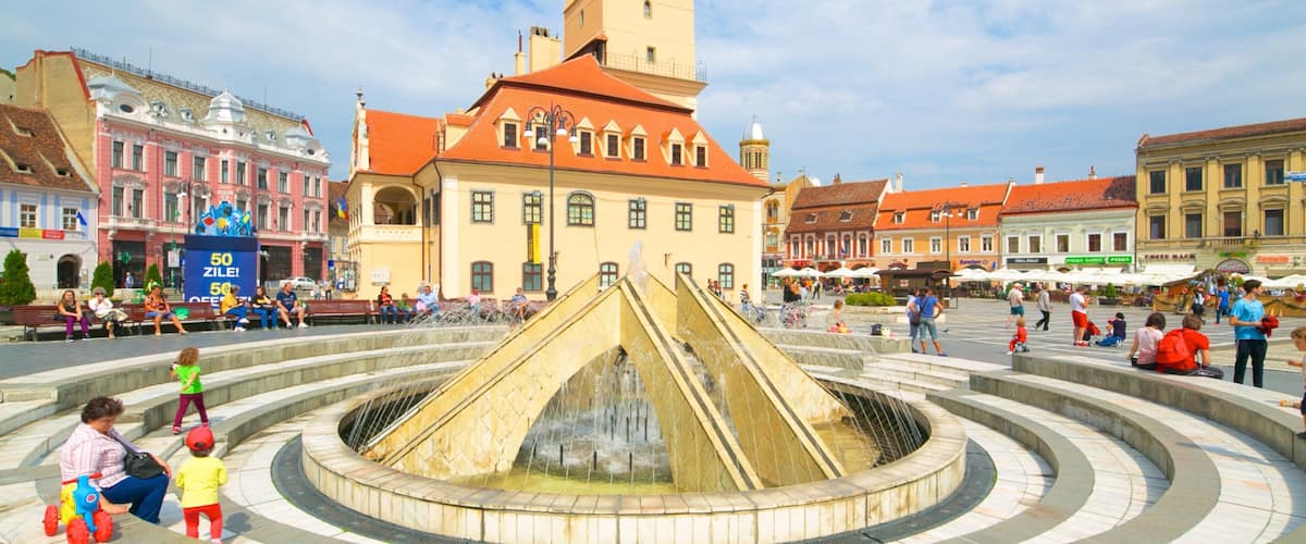 A historic square with a central fountain, a clock tower, and surrounding buildings.