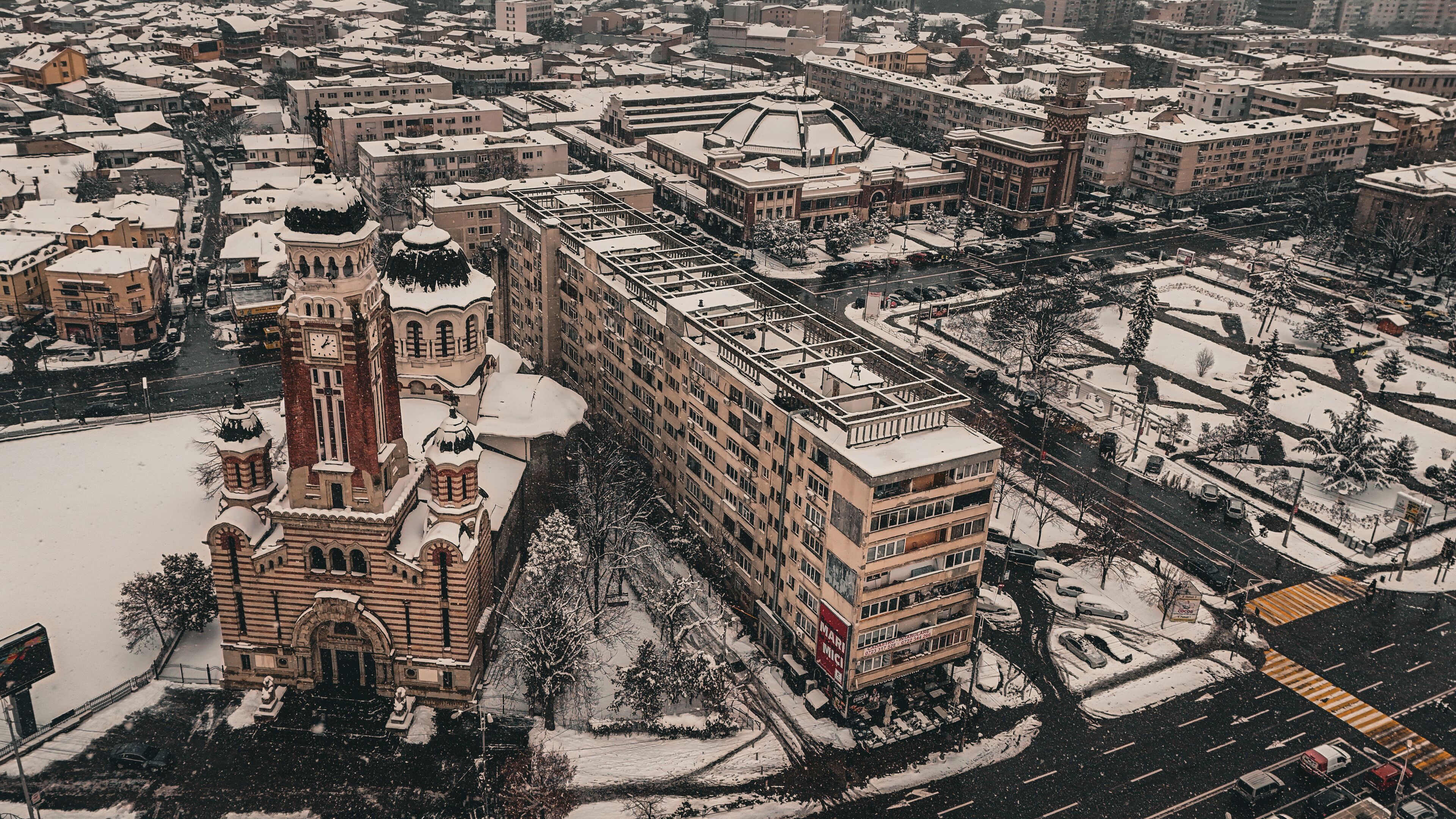 Un paisaje urbano cubierto de nieve con edificios históricos, incluyendo una iglesia destacada con una torre de reloj.