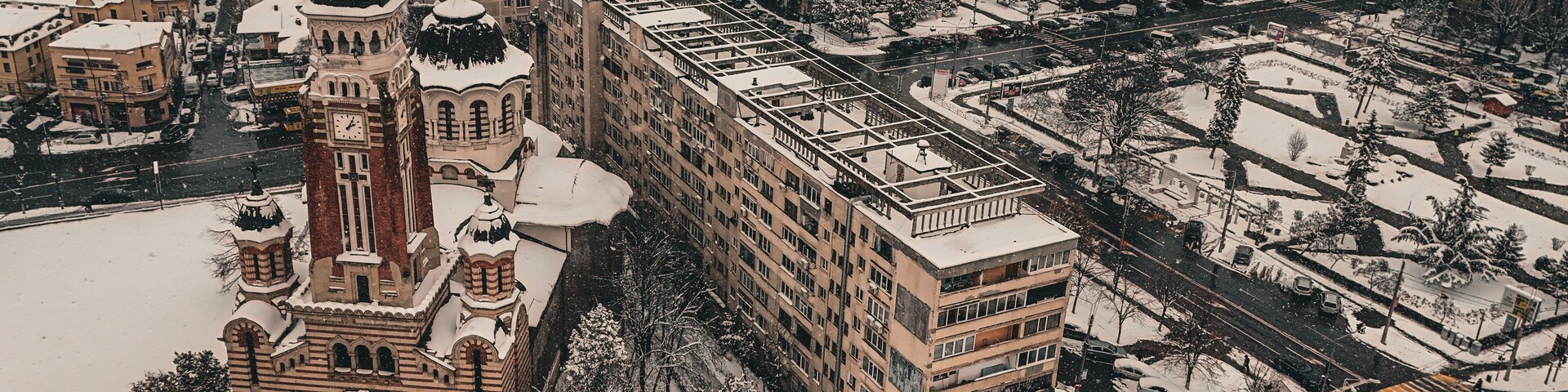 Un paisaje urbano cubierto de nieve con edificios históricos, incluyendo una iglesia destacada con una torre de reloj.
