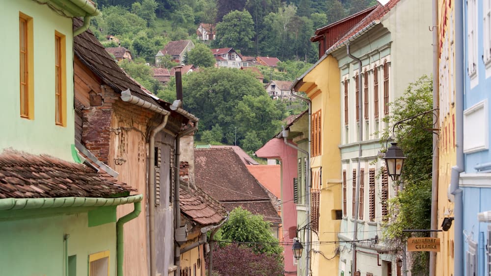 A narrow street with colorful buildings, a sign for 'ARTIZAMAT CERAMICA', and a hillside with houses in the background.