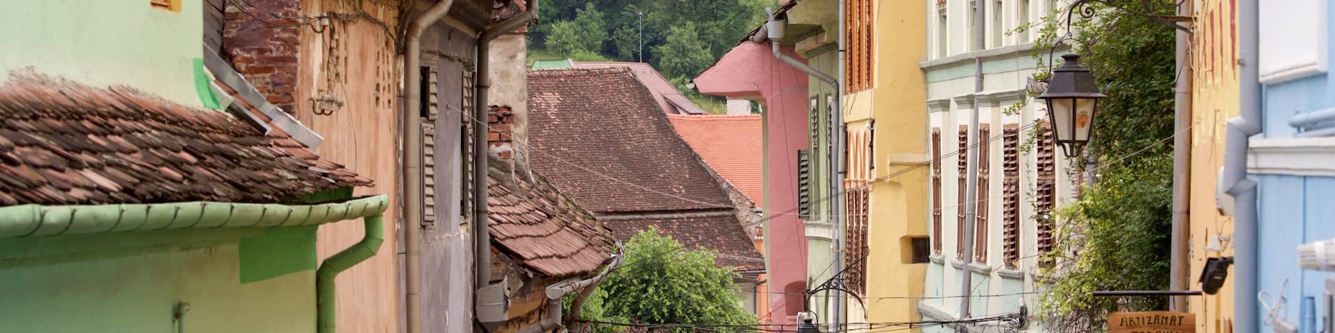 A narrow street with colorful buildings, a sign for 'ARTIZAMAT CERAMICA', and a hillside with houses in the background.